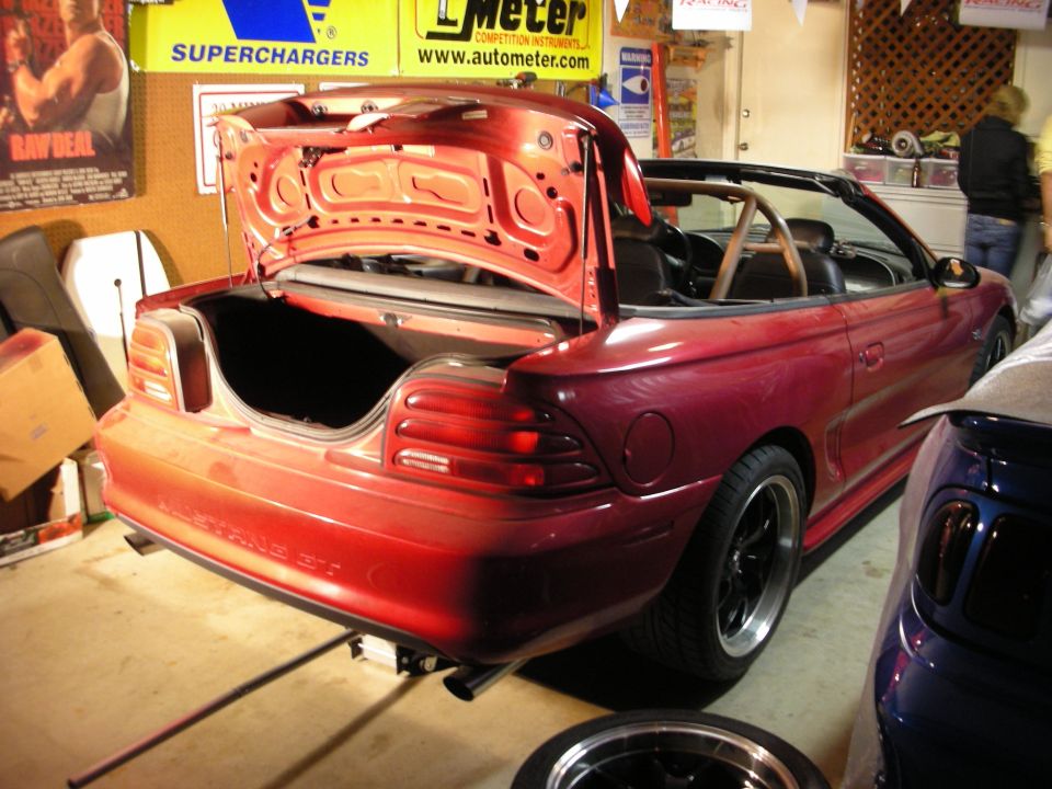 Red Mustang convertible with open trunk in a garage with banners