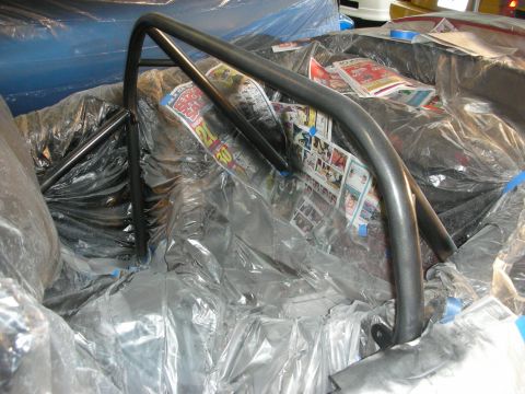1998 Ford Crown Victoria - black-painted tubular roll bar hoop mounted inside a car interior that is masked off with plastic sheeting and newspaper.