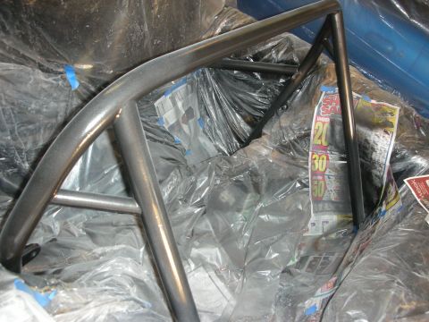 1998 Ford Crown Victoria - Bare metal welded roll cage tubing arches over a car interior covered in plastic sheeting and newspaper for painting.