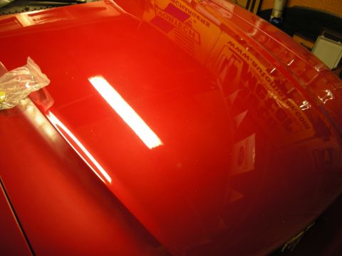 1998 Ford Crown Victoria - glossy red car hood reflects an overhead light and shop sponsor banners in its mirror-like paint.