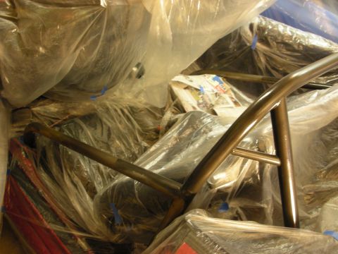 1998 Ford Crown Victoria - bent section of bare metal roll cage tubing sits over plastic-wrapped parts during a garage build.