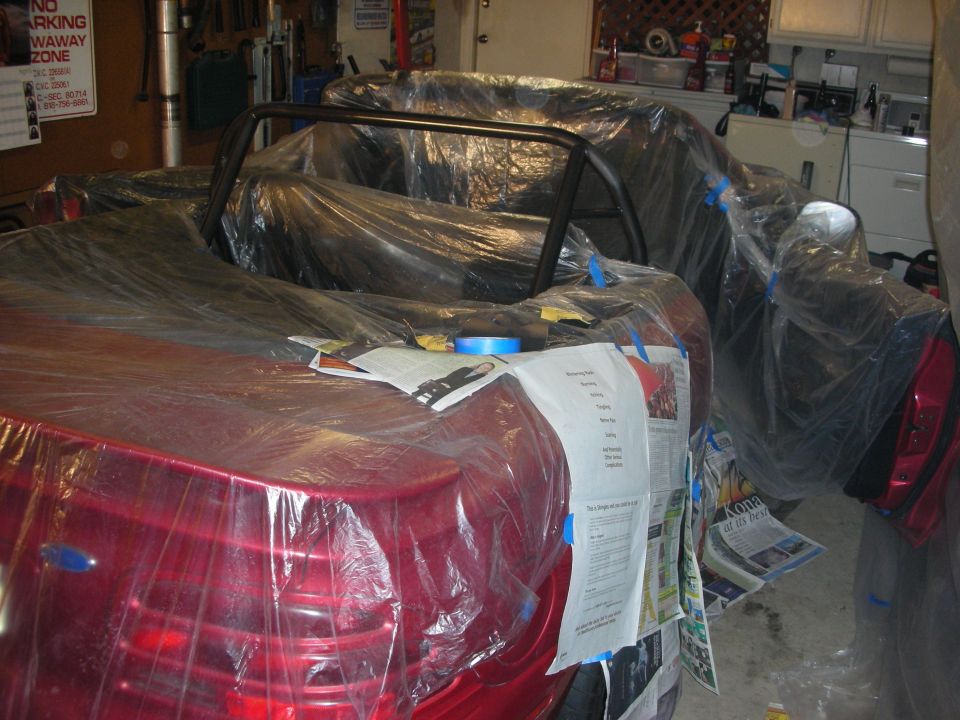 Red convertible masked in plastic with roll bar, papers on trunk, in a garage
