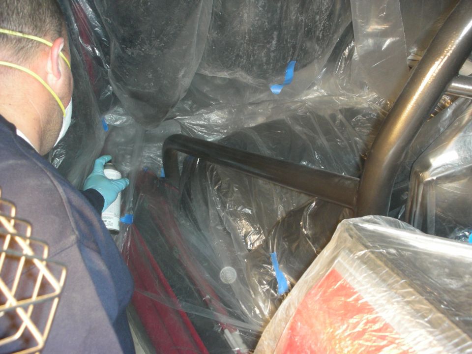Person in gloves working inside a plastic-masked car interior near a roll bar