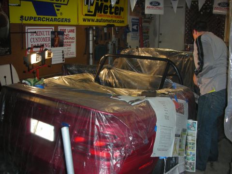 1998 Ford Crown Victoria - red convertible masked in plastic sits in a garage hung with Superchargers and AutoMeter banners as a person works at the rear.