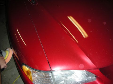 1998 Ford Crown Victoria - hand uses a buffer on the glossy red front fender of a car next to its headlight and amber marker at night.