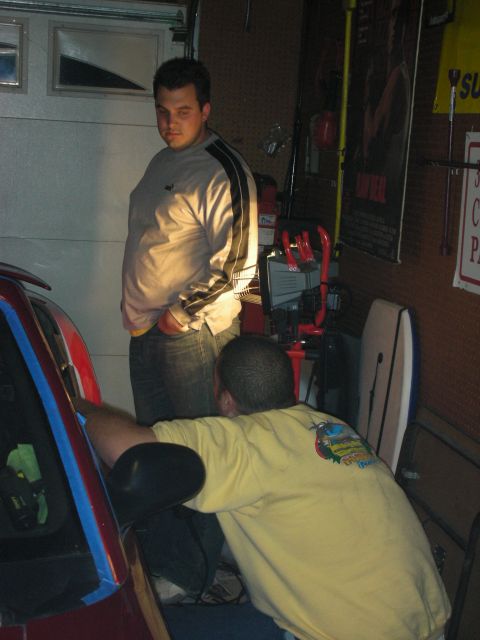 1998 Ford Crown Victoria - Two men work near a red car in a garage at night, one standing and one crouched over the fender by a tool chest.