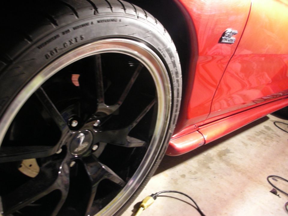 Close-up of black multi-spoke wheel and tire on orange-red sports car in garage