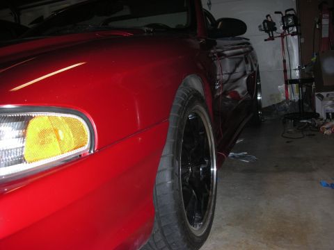 1998 Ford Crown Victoria - Low front-corner view of a red car showing an amber headlight lens and black wheel inside a cluttered garage.