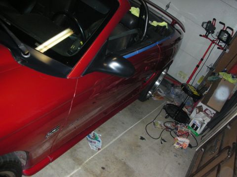 1998 Ford Crown Victoria - Side view of a red Mustang convertible with the top down parked in a garage amid scattered tools and supplies.