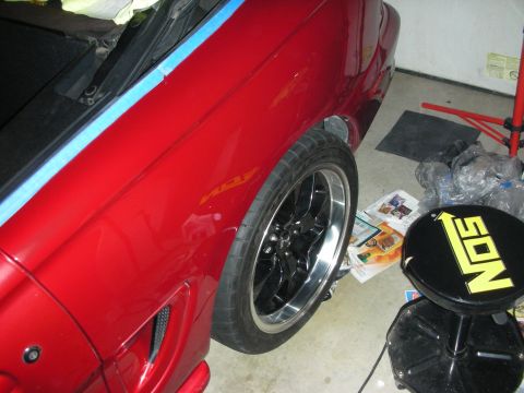 1998 Ford Crown Victoria - Rear quarter of a red convertible with a black wheel in a garage, with a yellow NOS-branded bar stool nearby.