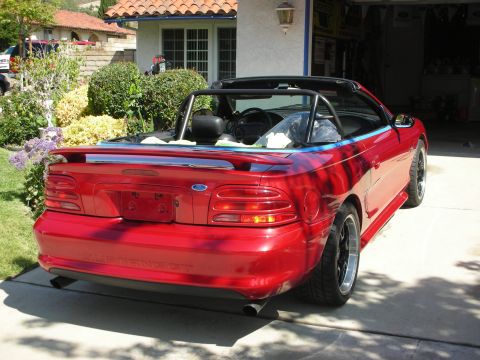 1998 Ford Crown Victoria - Rear three-quarter view of a red Ford Mustang convertible parked in a driveway in front of a Spanish-style stucco home.