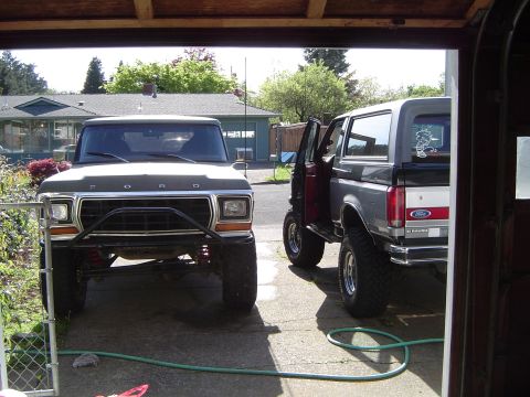 1978 Ford Bronco - Two Ford Broncos are parked in a driveway, one with its door open.