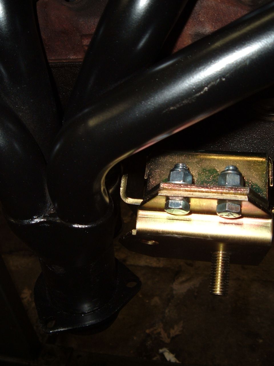 Black exhaust header tubes beside a gold-plated engine mount bracket with bolts and stud