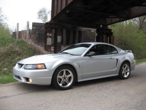 1998 Ford Taurus - This silver coupe, likely a Ford Mustang from the early 2000s, is parked beneath a railway bridge.