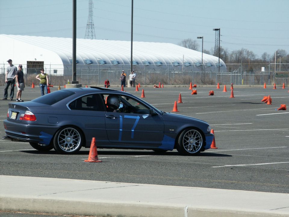 Dark blue BMW 3 Series coupe with blue tape accents and large '17' on the door, driving on a course with orange cones