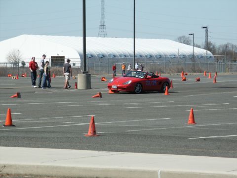 2001 Mercury Grand Marquis - A red convertible sports car with racing numbers is positioned on a paved lot marked with orange cones, likely for an event.