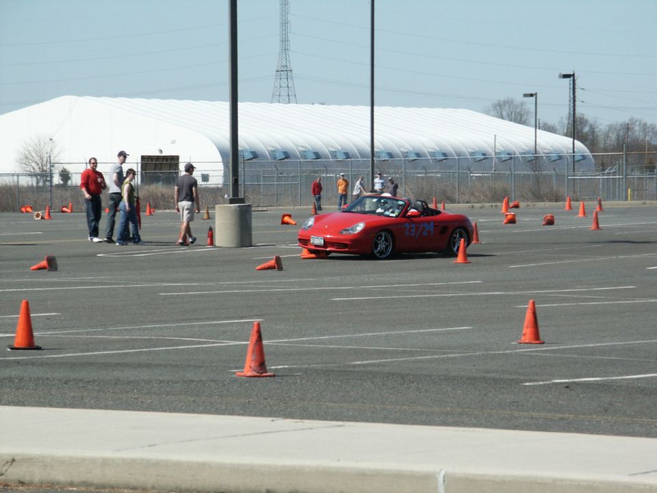 Red convertible sports car with racing numbers 23/24 on side, parked on a course with orange cones