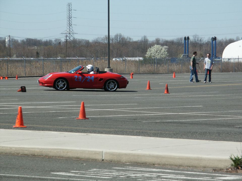 Red convertible sports car with racing numbers 23/24 on the door, driving on a paved track with orange cones
