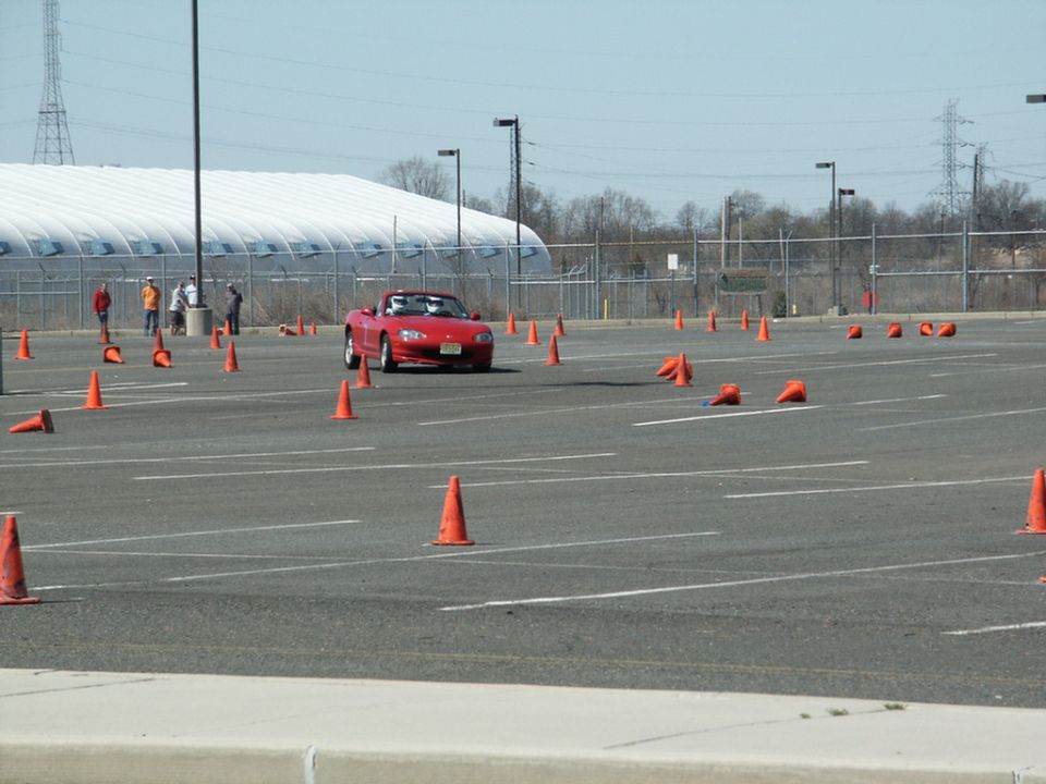 Red convertible sports car driving through an autocross course marked by orange cones