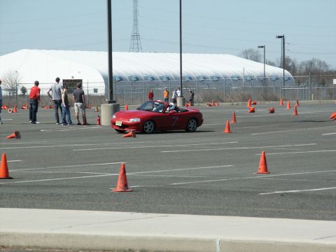 2001 Mercury Grand Marquis - Red Mazda Miata navigates an autocross course with cones and spectators present.