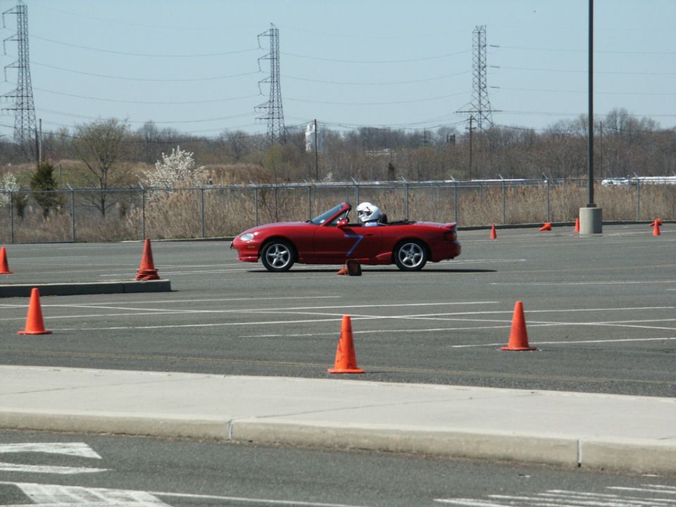 Red convertible sports car with driver in helmet navigating a cone course
