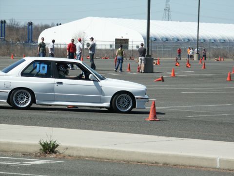 2001 Mercury Grand Marquis - A white BMW E30 coupe navigates an autocross course marked by orange cones, with spectators in the background.