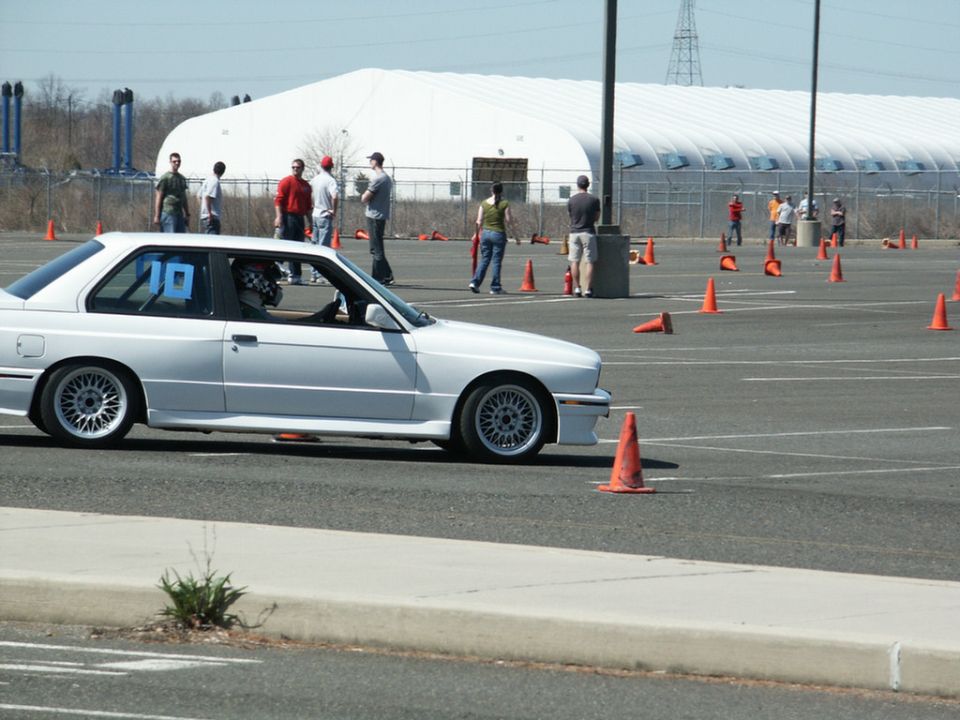 White BMW E30 coupe with number 19 on window driving through autocross course with orange cones