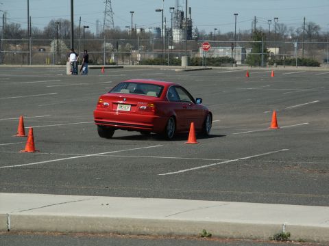 2001 Mercury Grand Marquis - A red BMW coupe is seen maneuvering through an autocross course marked by orange cones in an empty parking lot.