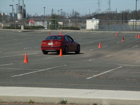 2001 Mercury Grand Marquis - A red sedan maneuvers through an autocross course marked by orange cones in a large parking lot.