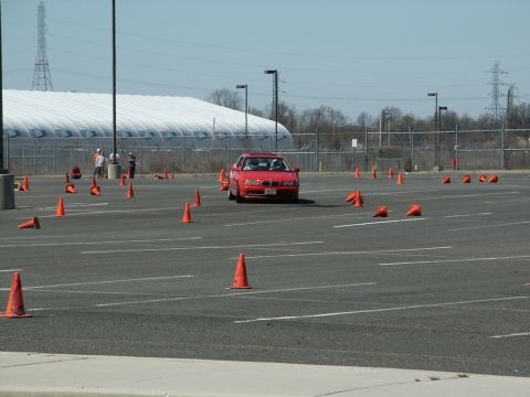 2001 Mercury Grand Marquis - A red BMW sedan navigates a course marked by orange cones in an open parking lot under a clear sky.