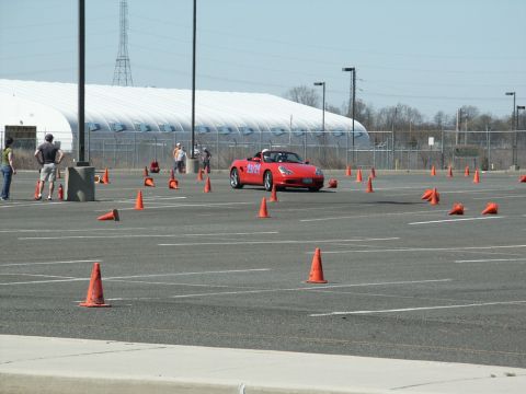 2001 Mercury Grand Marquis - A red convertible sports car with racing numbers on its door navigates a cone course in a parking lot.