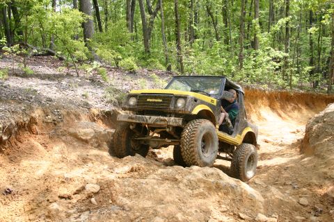 1990 Suzuki Samurai - A yellow Suzuki Samurai navigates a challenging off-road trail with steep inclines and loose dirt.