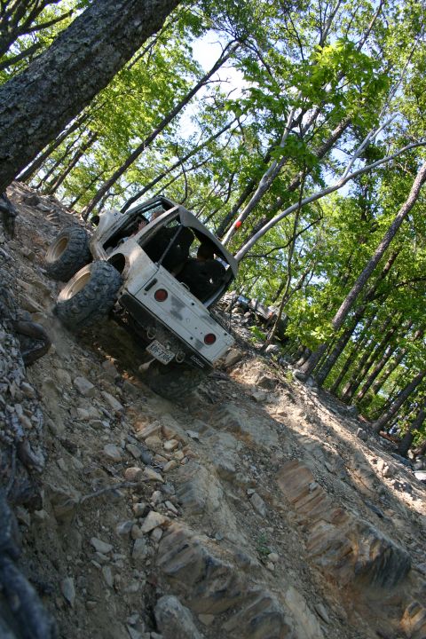 1990 Suzuki Samurai - This off-road vehicle navigates a challenging, steep, rocky terrain surrounded by trees.