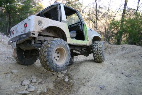1990 Suzuki Samurai - Mud-covered 1990 Suzuki Samurai navigates a rough dirt path with large tires.