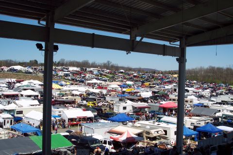 2001 Ford Crown Victoria - A wide view of a bustling outdoor market filled with vehicles and tents on a sunny day.