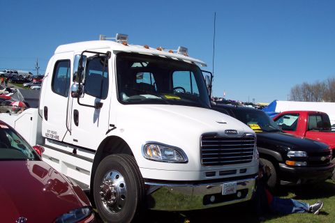 2001 Ford Crown Victoria - A white tow truck is parked at an outdoor event, with other vehicles visible in the background.