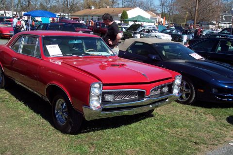 2001 Ford Crown Victoria - A red 1966 Pontiac GTO is parked on grass next to a dark blue convertible at an outdoor car show.