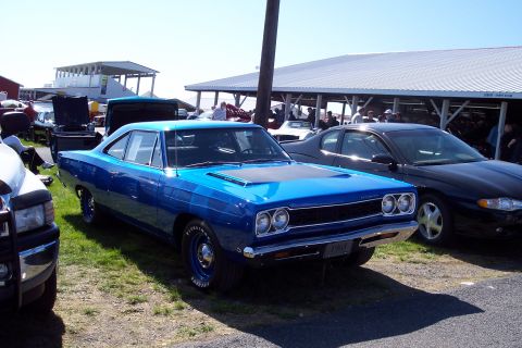 2001 Ford Crown Victoria - A blue classic Plymouth Road Runner is displayed at an outdoor car show with other vehicles and spectators in the background.
