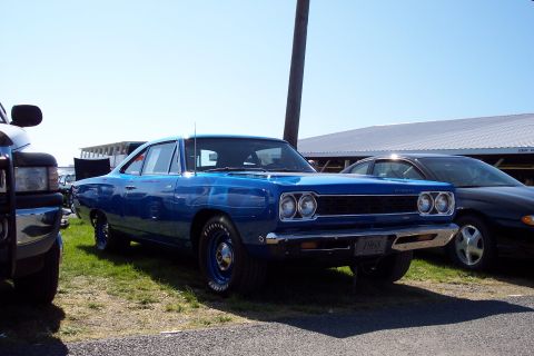 2001 Ford Crown Victoria - A blue 1968 Plymouth Road Runner is parked at an outdoor event, with a black sedan visible behind it.