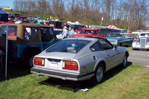 2001 Ford Crown Victoria - A silver Datsun 280Z is parked on grass at an outdoor car show with other vehicles visible in the background.