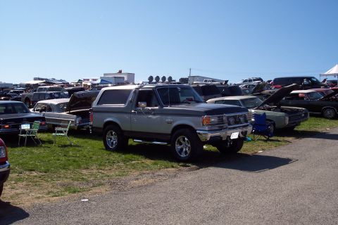 2001 Ford Crown Victoria - A two-tone Ford Bronco is prominently displayed among other vehicles at an outdoor event.