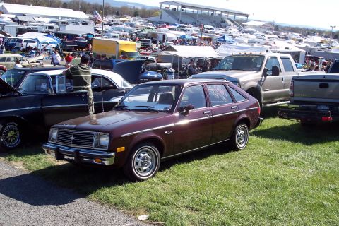 2001 Ford Crown Victoria - A maroon hatchback is parked on the grass at an outdoor event with many tents and vehicles in the background.