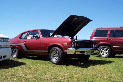 2001 Ford Crown Victoria - Red 1975 Chevrolet Nova coupe at a car show with hood open, parked next to other vehicles.