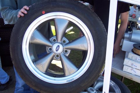 2001 Ford Crown Victoria - A person holds up a silver five-spoke Ford wheel with a tire mounted on it.