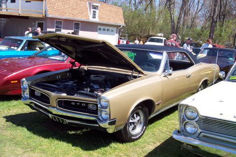2001 Ford Crown Victoria - A gold 1966 Pontiac GTO convertible is displayed with its hood open at an outdoor car show.
