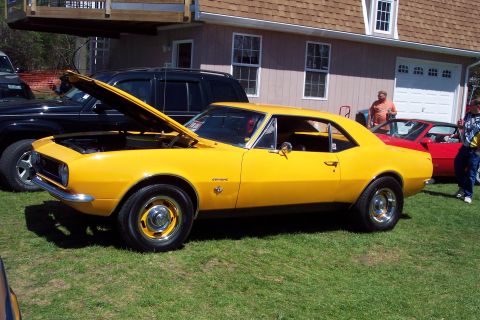 2001 Ford Crown Victoria - A yellow 1967 Chevrolet Camaro is displayed outdoors with its hood up, alongside other vehicles.