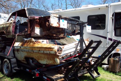 2001 Ford Crown Victoria - A heavily rusted car body, appearing to be from the early 1960s, is loaded onto a trailer, with a white RV parked behind it.