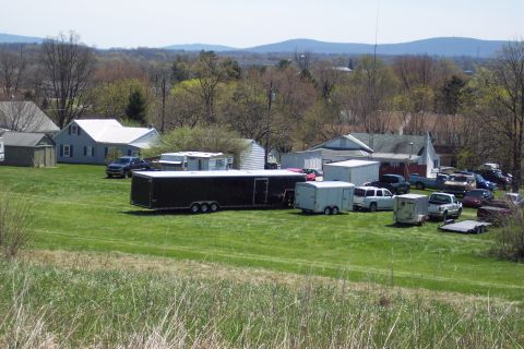 2001 Ford Crown Victoria - A collection of vehicles and trailers are parked in a grassy area with houses and trees in the background.