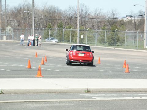 2001 Mercury Grand Marquis - A red Mini Cooper navigates a cone course in an open parking lot with spectators in the background.