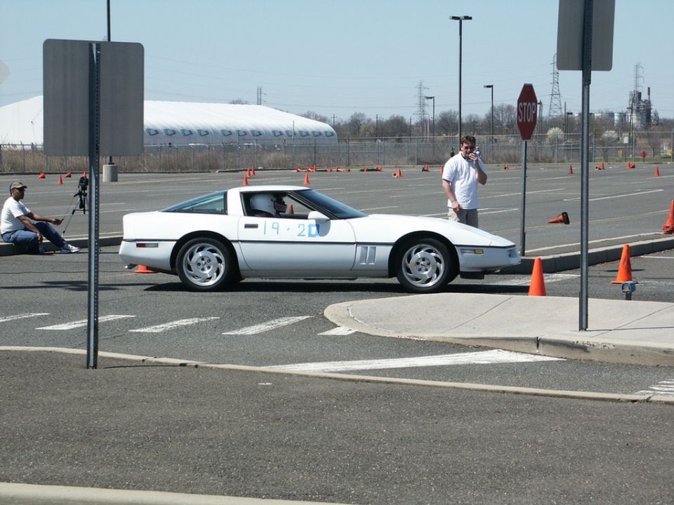 White Chevrolet Corvette with "19 20" written on the door, parked on asphalt with orange cones